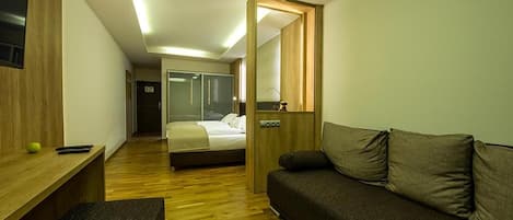 A modern hotel room with a wooden floor, a bed, a sofa, a desk, and a mirror.