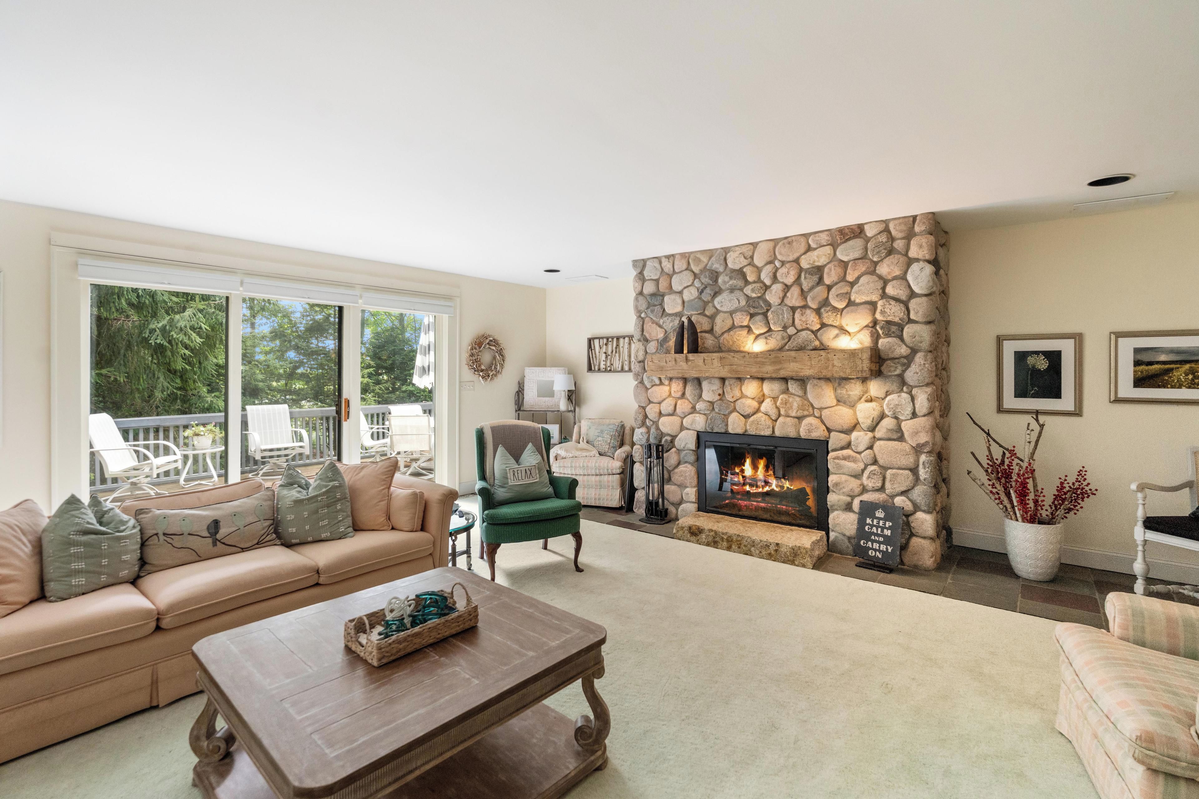 Una sala de estar con chimenea de piedra, un sillón verde, un sofá color beige y una mesa de centro.