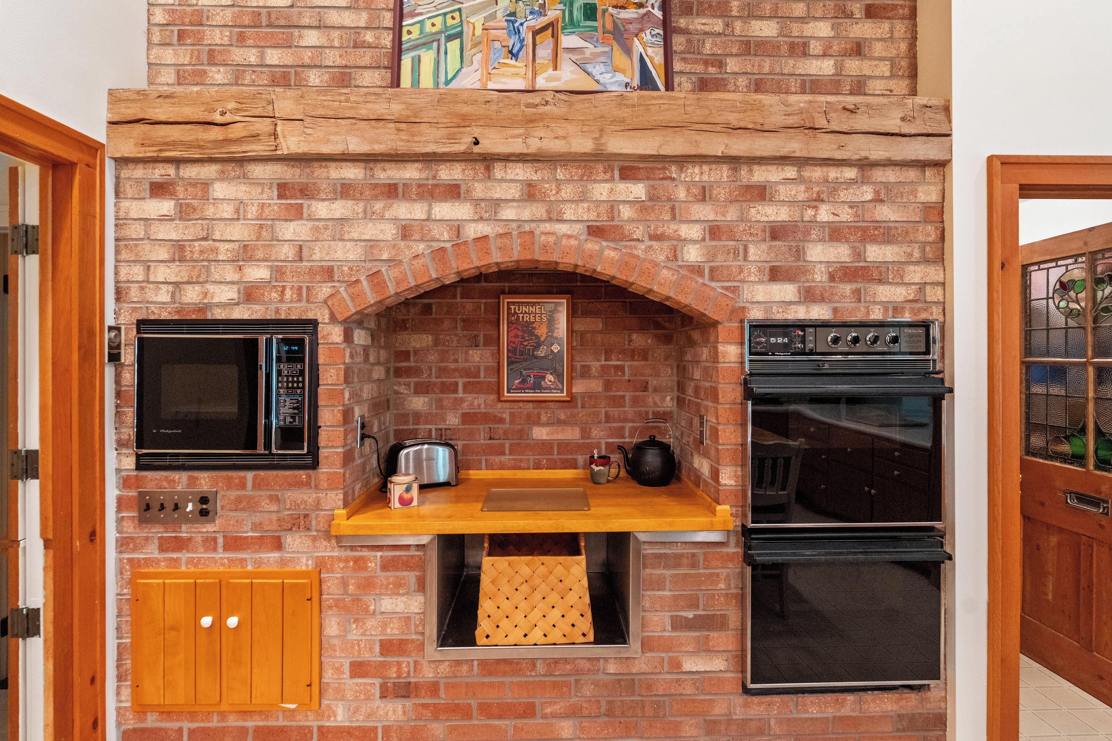 A kitchen with a brick wall, a microwave, a toaster, a kettle, and a stove.
