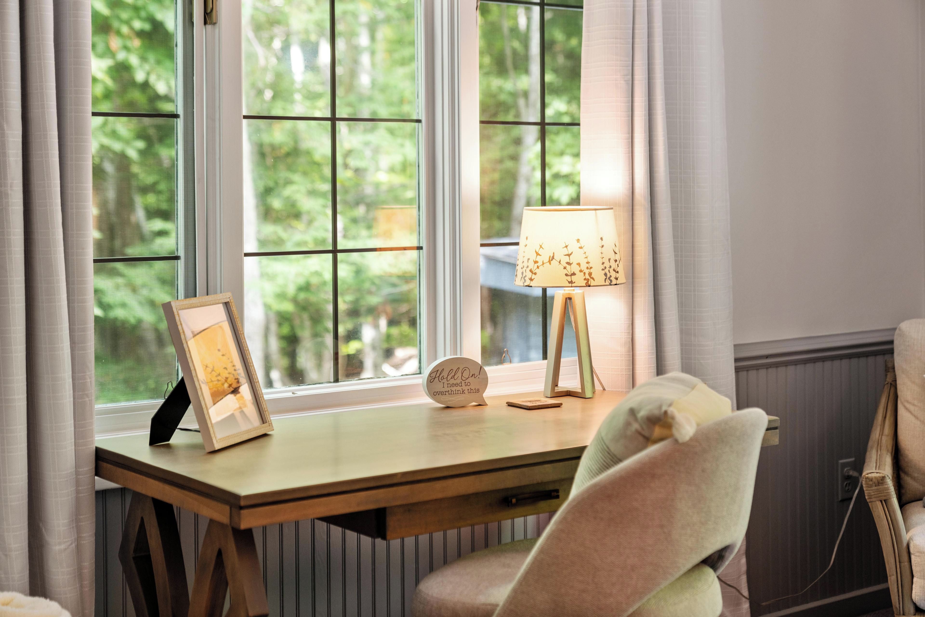 Un bureau en bois, une lampe, un tableau encadré et un petit panneau avec du texte.