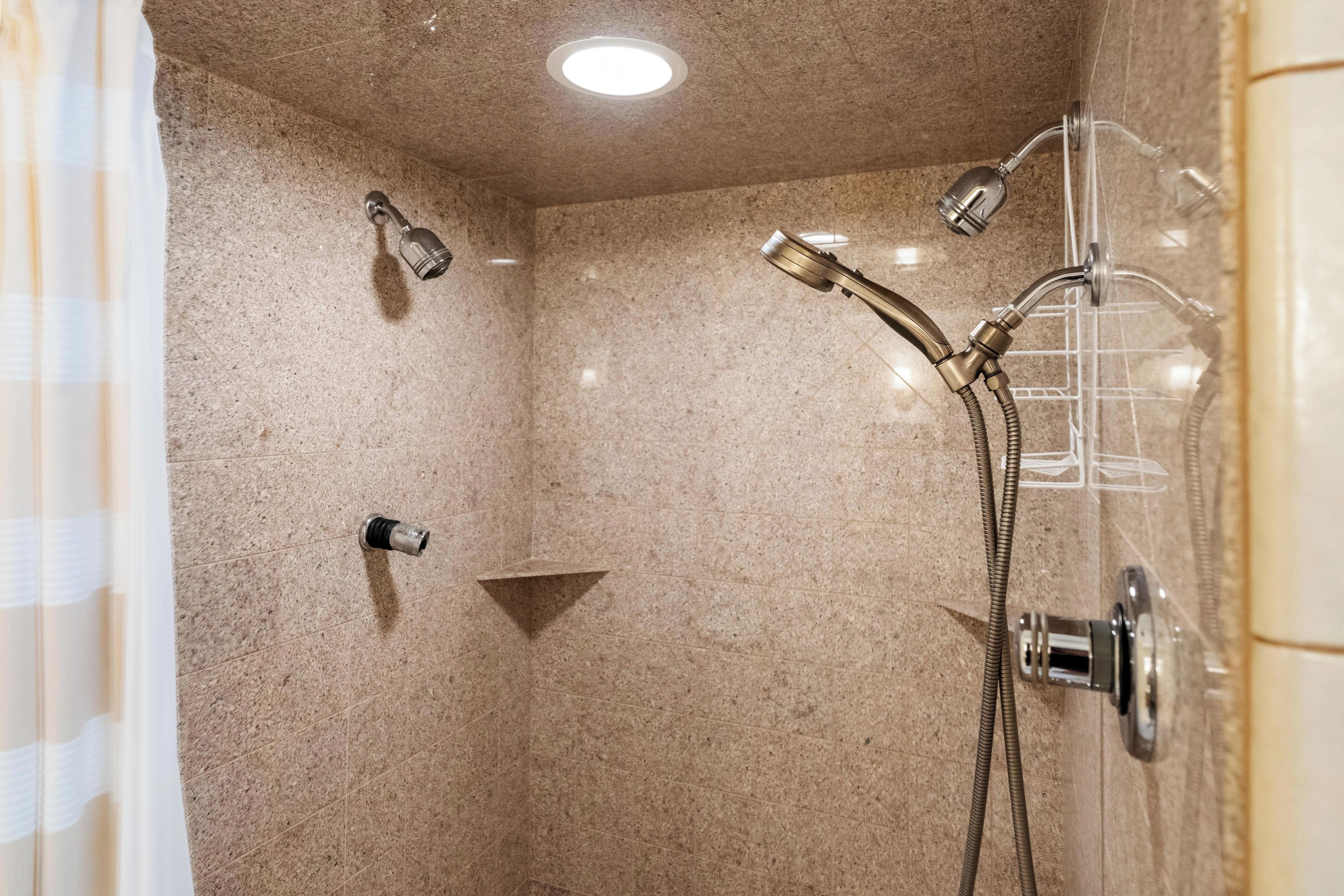 A shower with a handheld showerhead, a wall-mounted showerhead, and a handheld shower attachment.