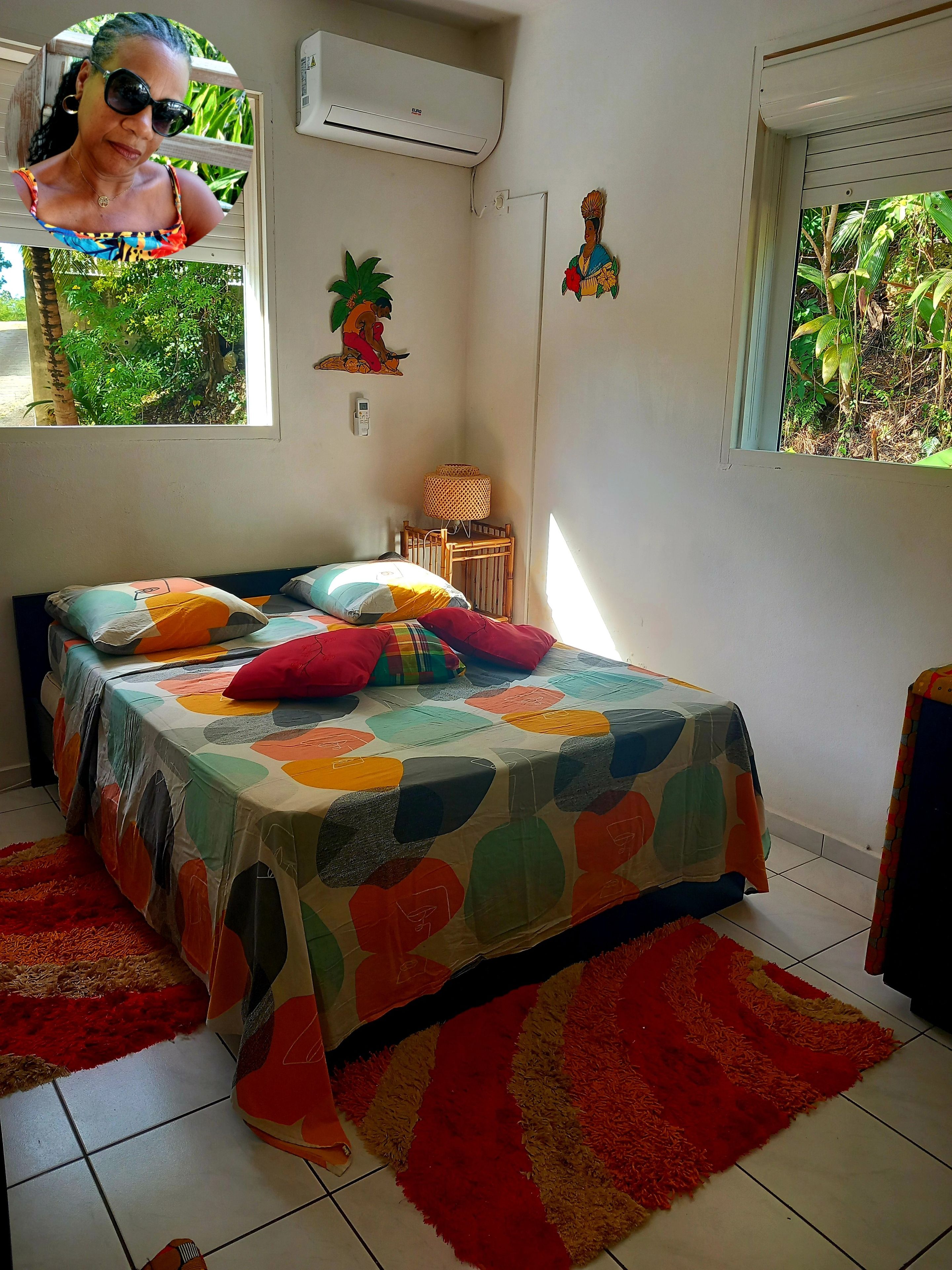 Une chambre à coucher avec un lit, une fenêtre, un climatiseur fixé au mur et une petite table avec une lampe.