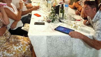 En grupp människor sitter runt ett bord med en vit duk, olika glas, flaskor och en smartphone på bordet.