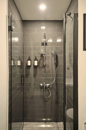 A modern bathroom with a glass shower enclosure, a handheld showerhead, and two bottles of shampoo on the wall. - Modern 2br, Living Areas, 2 Baths, Kadıköy (Istanbul)