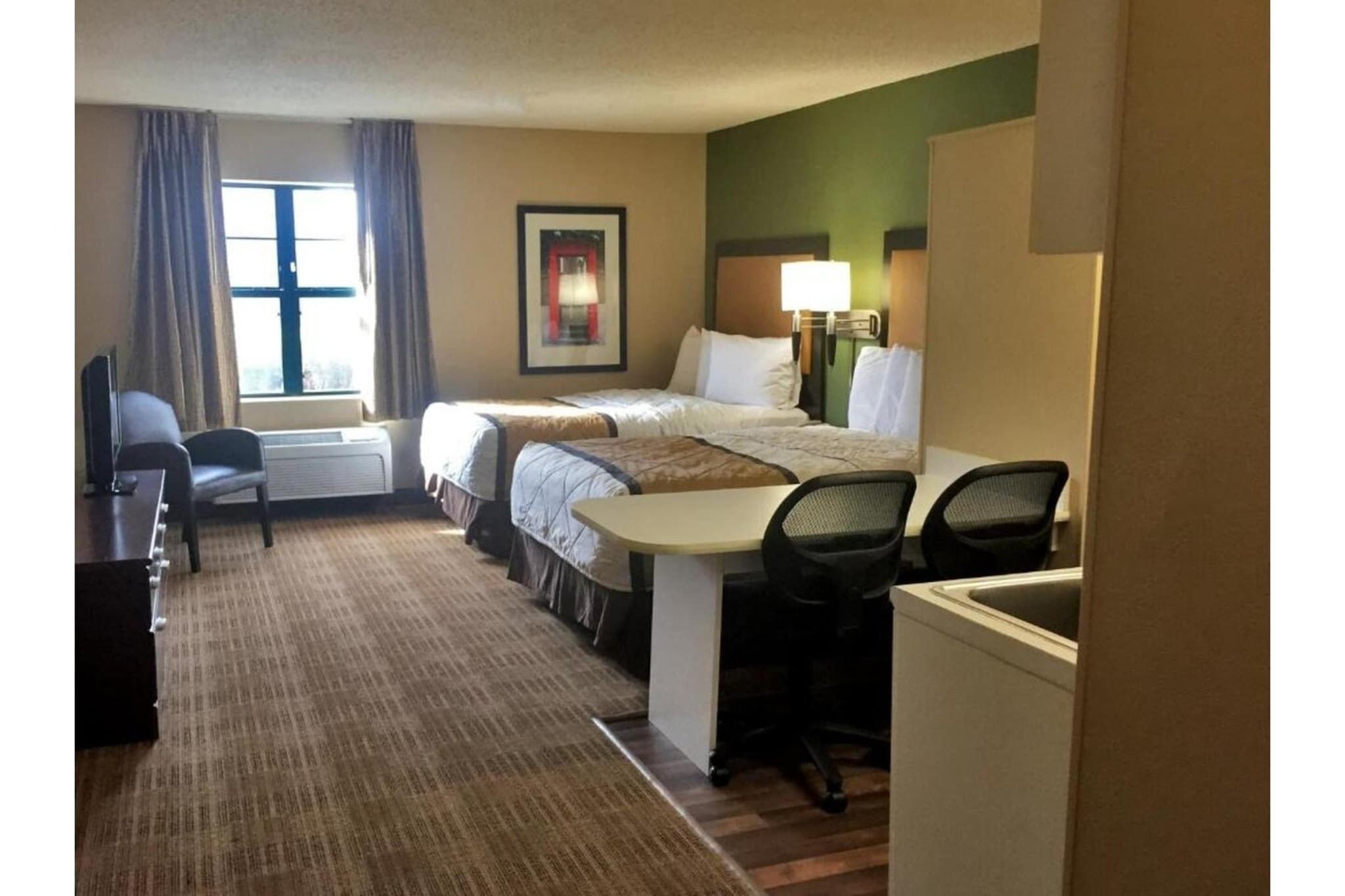 Quarto de hotel com duas camas, uma escrivaninha, uma cadeira, uma televisão e uma janela com cortinas.