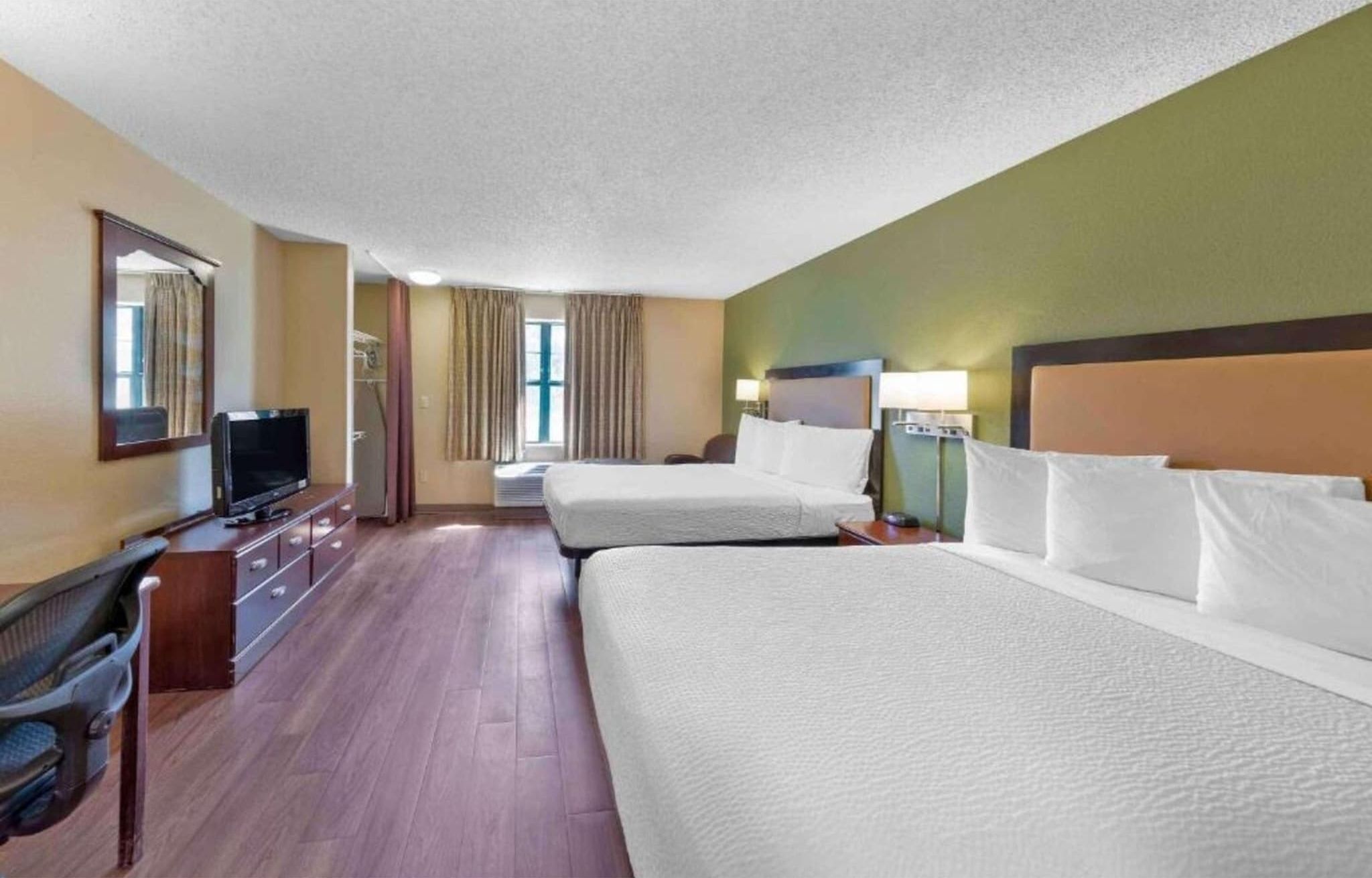 Een hotelkamer met twee bedden, een bureau met een televisie en een raam met gordijnen.
