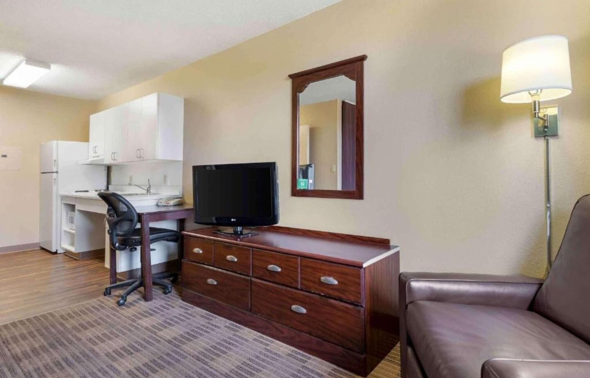 A hotel room with a desk, chair, television, dresser, and a sofa.