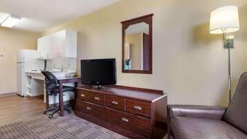A hotel room with a desk, chair, television, dresser, and a sofa.