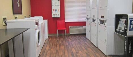 A laundry facility with multiple washing machines, a red wall, and a USA Today newspaper dispenser.