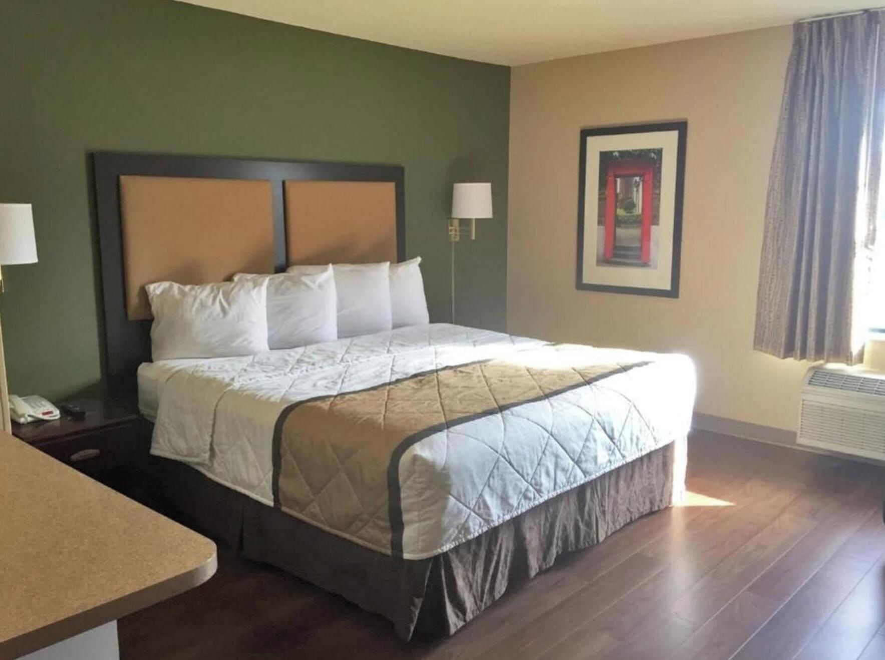 A hotel room with a bed, bedside table, lamp, and a framed picture on the wall.