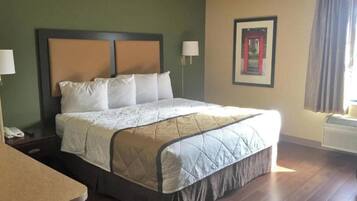A hotel room with a bed, bedside table, lamp, and a framed picture on the wall.