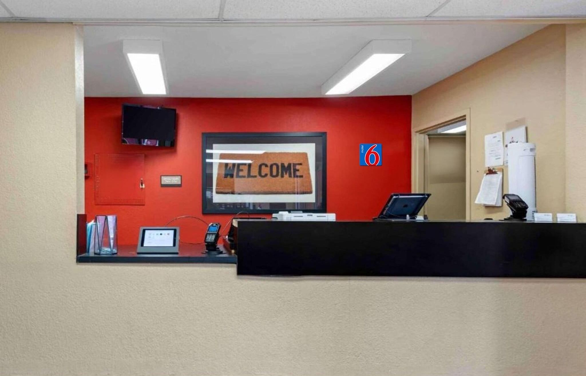 A reception desk with a 'WELCOME' sign, a television, a phone, and a computer.