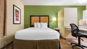 Ein Hotelzimmer mit Bett, Schreibtisch, Stuhl, Lampe und einem gerahmten Bild an der Wand.