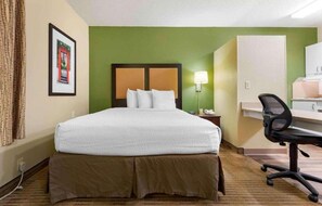 A hotel room with a bed, a desk, a chair, a lamp, and a framed picture on the wall. - 1 Queen Bed | Non-Smoking, Kitchen (Rochester NY)