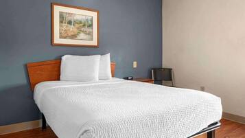 A neatly made bed with a white bedspread in a room with a blue wall and a framed picture above it.