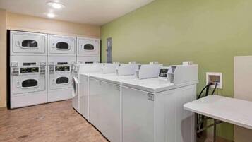 A laundry room with multiple washing machines and dryers, a control panel, and a table.