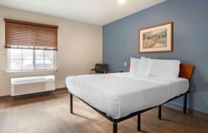 A bedroom with a bed, a window with blinds, a radiator, a chair, and a painting on the wall. - 1 Full Bed | Non-Smoking, Kitchen (Cincinnati OH)