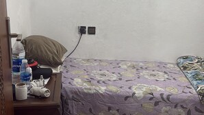 A small, simple room with a bed, a nightstand, and a wall socket. - DAR LALLA KHADIJA (RABAT)