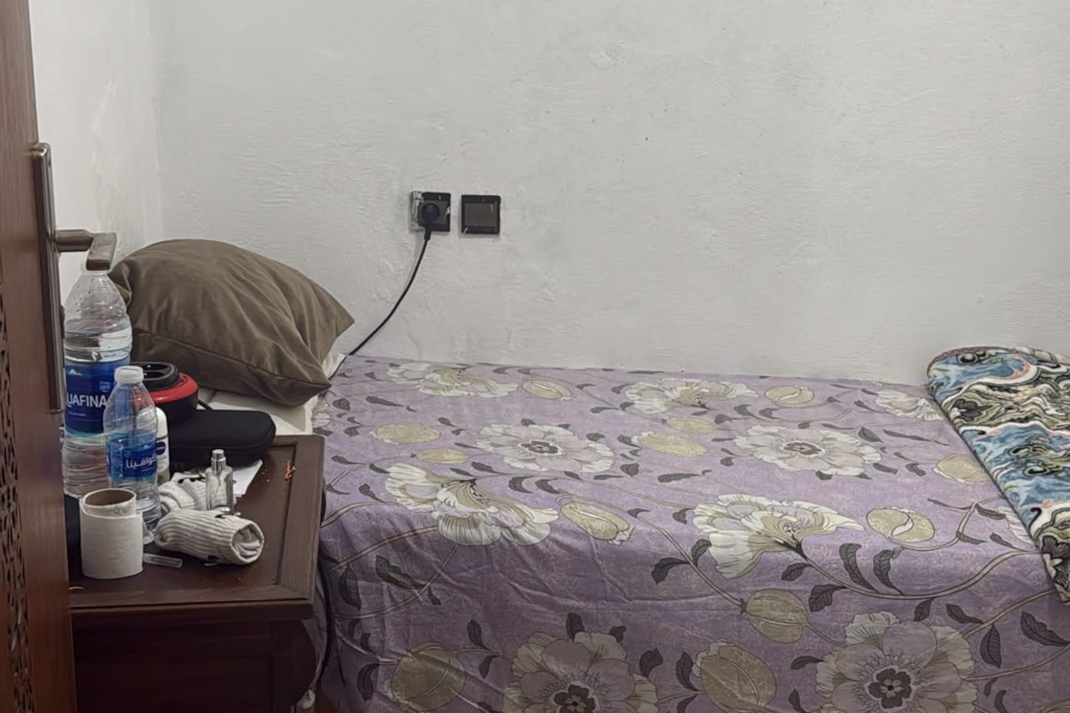 A small, simple room with a bed, a nightstand, and a wall socket.