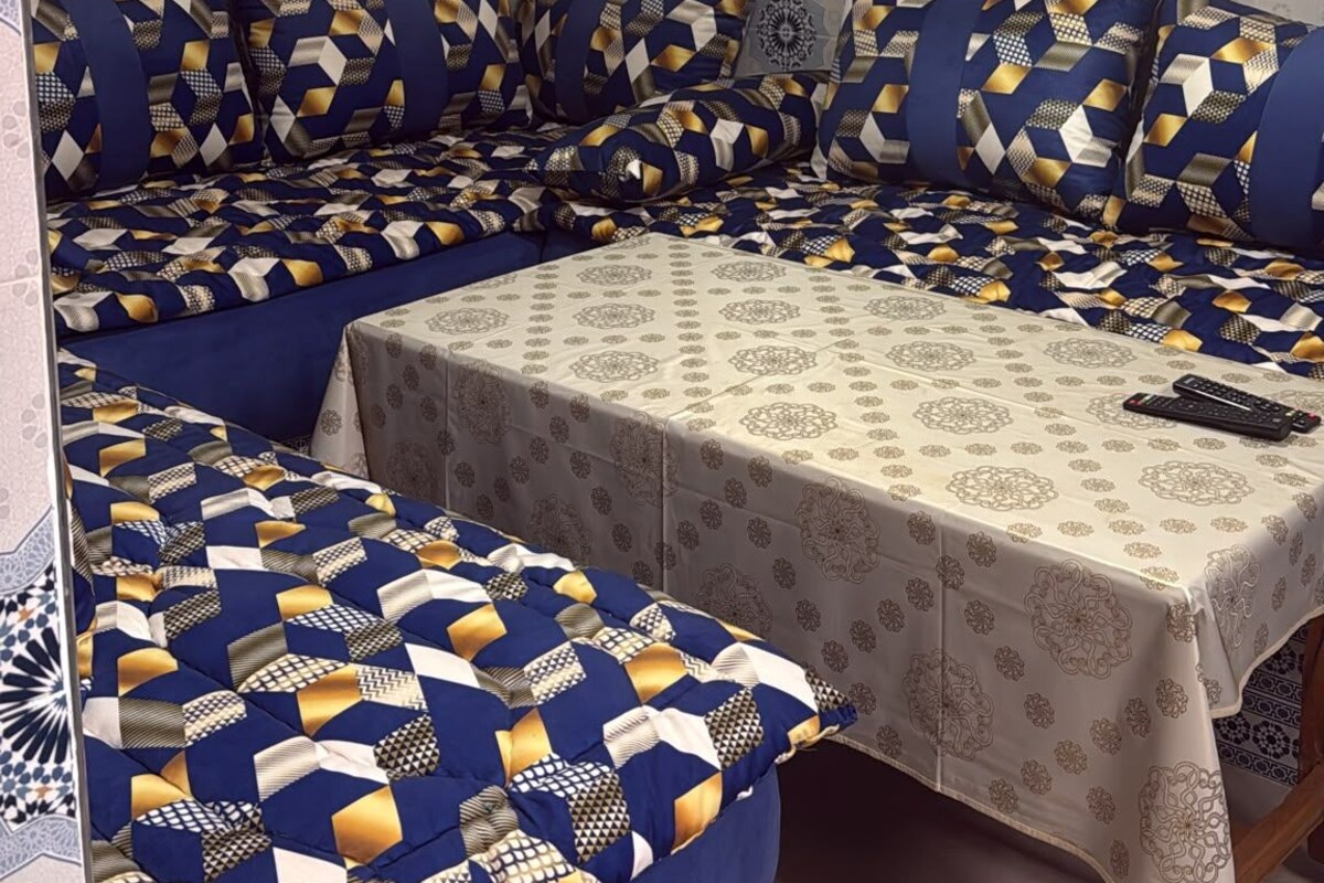 A room with a sofa set, a table with a patterned tablecloth, and a decorative ceiling light.