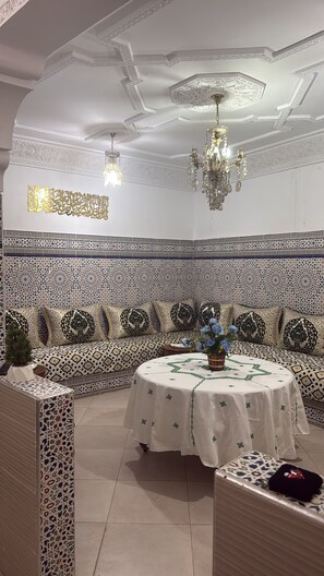 A room with a patterned wall, a round table with a white tablecloth, and two hanging chandeliers. - DAR LALLA KHADIJA (RABAT)