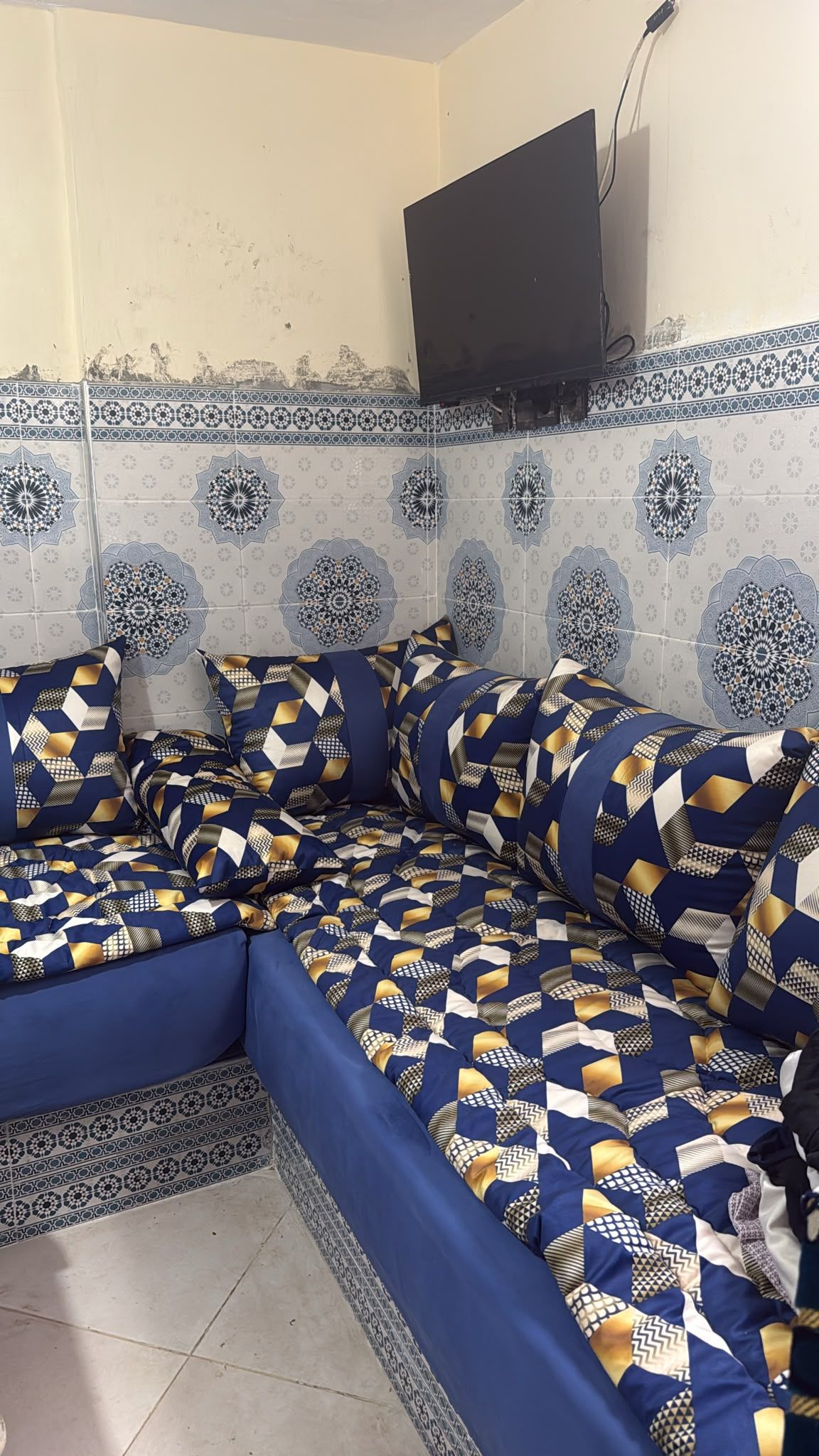 Une pièce avec un canapé d’angle, des carreaux décoratifs et un téléviseur fixé au mur.