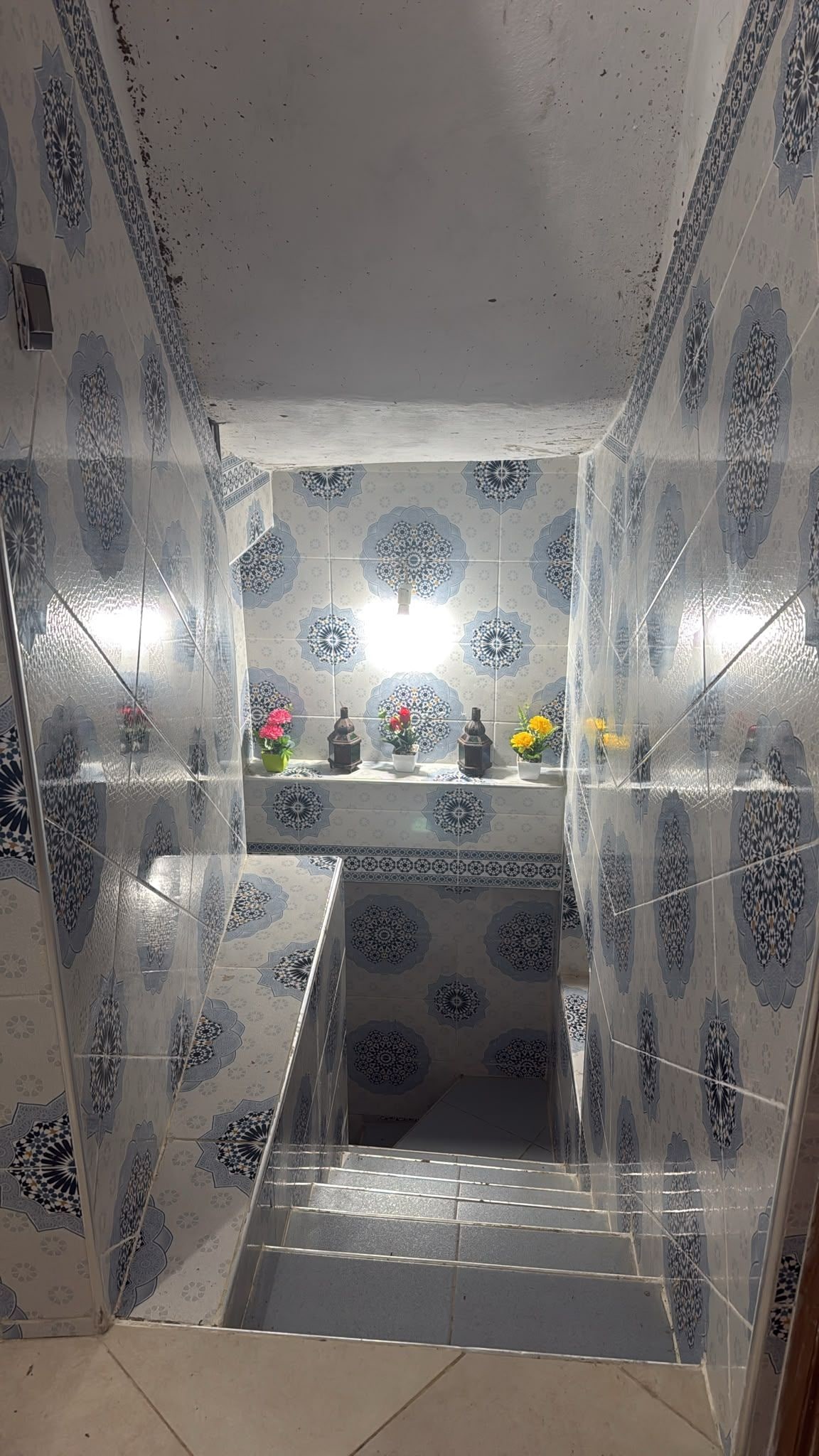 Un baño con piso y paredes de azulejos, un lavamanos con espejo y una ventana.