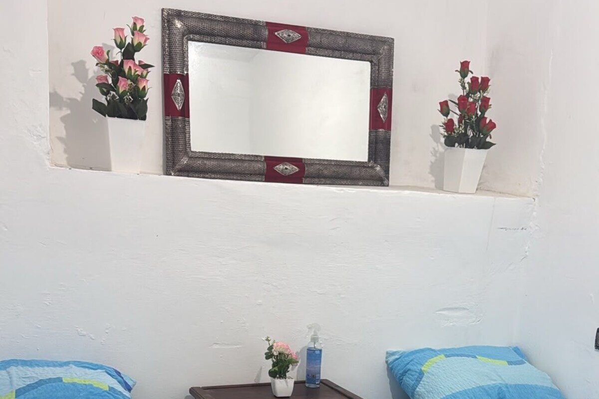 A bedroom with two beds, a dresser, a mirror, and a small shelf with flowers.