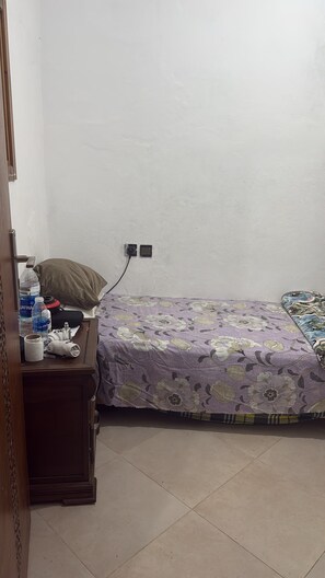 A small, simple room with a bed, a nightstand, and a wall socket. - DAR LALLA KHADIJA (RABAT)