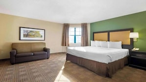 Een hotelkamer met een bed, een bank, een raam met gordijnen, een schilderij aan de muur en een nachtkastje met een lamp.