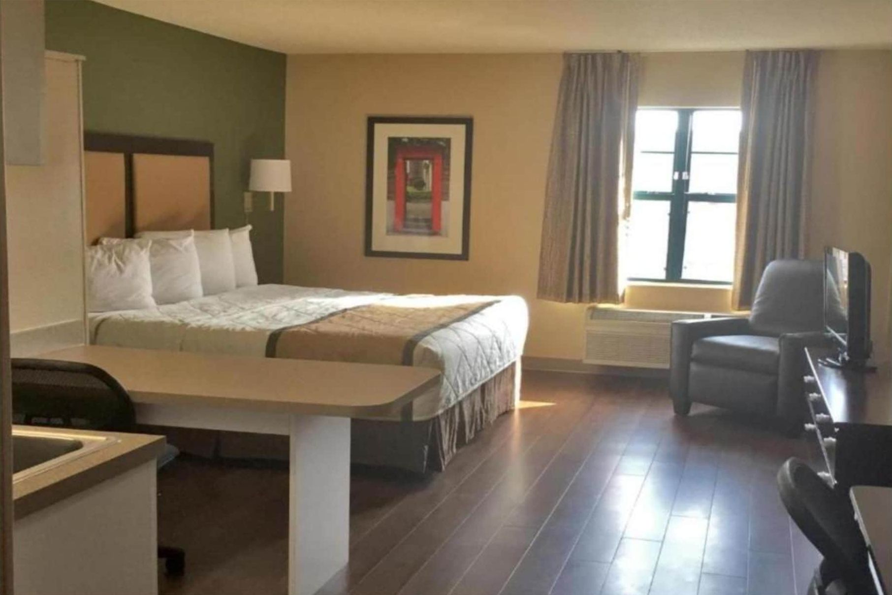 A hotel room with a bed, a desk, a chair, a television, and a window with curtains.
