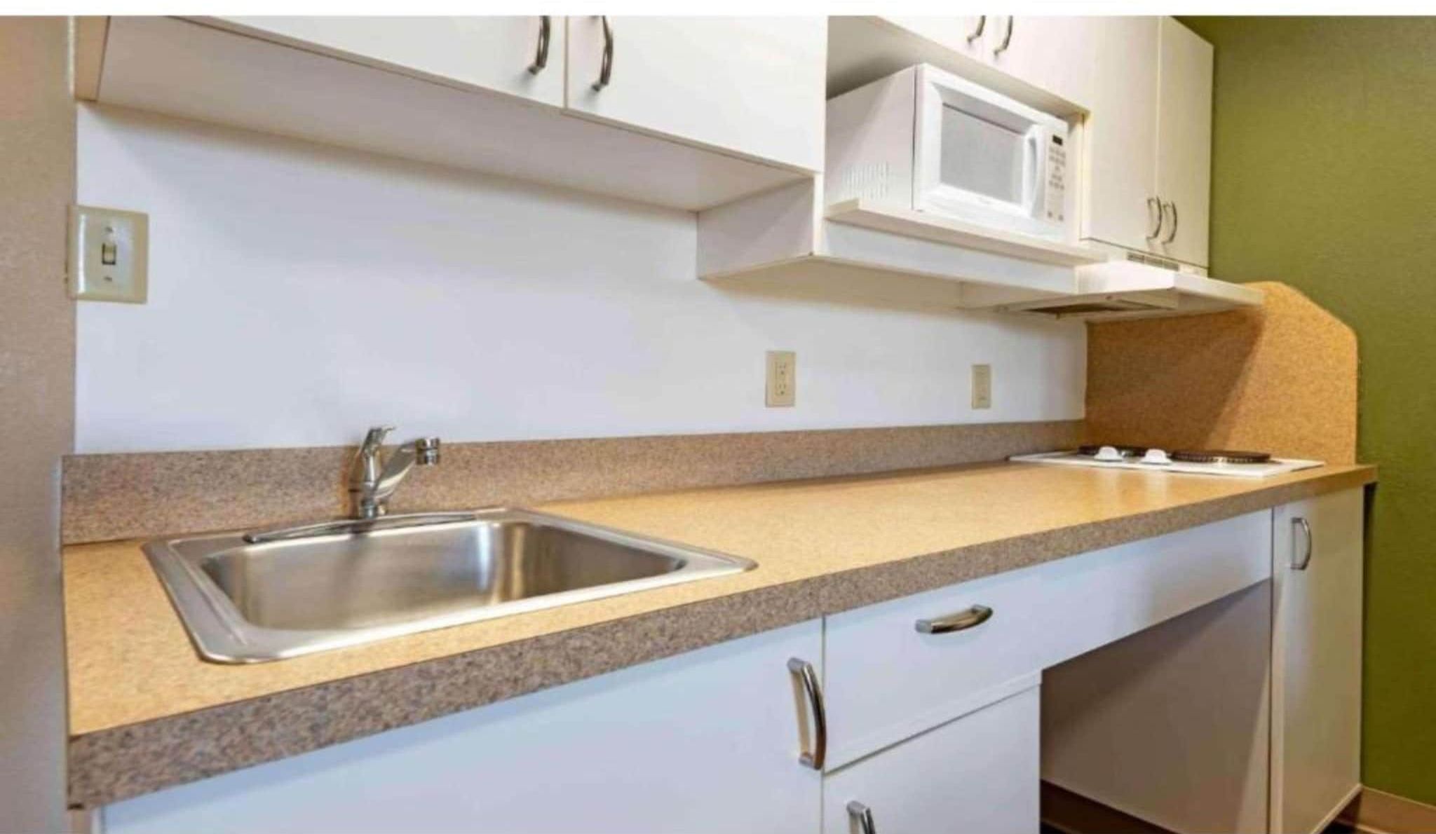A kitchen with a double sink, white cabinets, a microwave, and a gas stove.