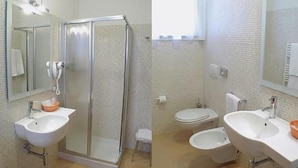 Et badeværelse med en brusekabine med glasvægge, to håndvaske og et toilet.