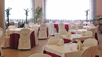 Un salón de banquetes con mesas redondas, sillas y vista al mar a través de amplios ventanales.
