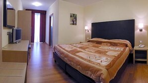 Et hotelværelse med seng, sengeborde med lamper, et skrivebord med computer og et fjernsyn.