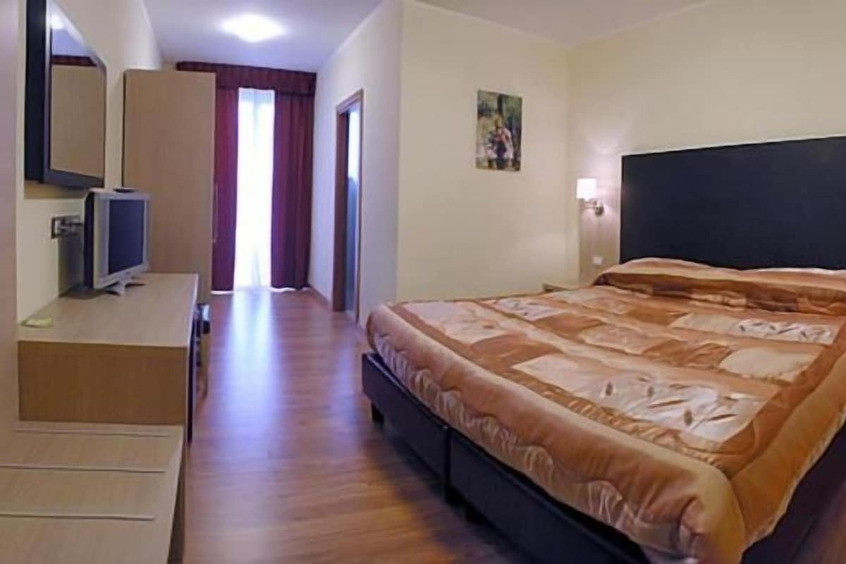 Una habitación de hotel con una cama, lámparas de noche, un escritorio con una computadora y un televisor.