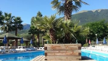 Um banco de madeira junto a uma piscina, com palmeiras e uma montanha ao fundo.