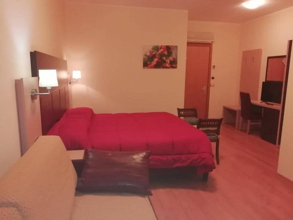 Una camera d'albergo con un letto, una scrivania, una sedia, una TV e un quadro appeso al muro.