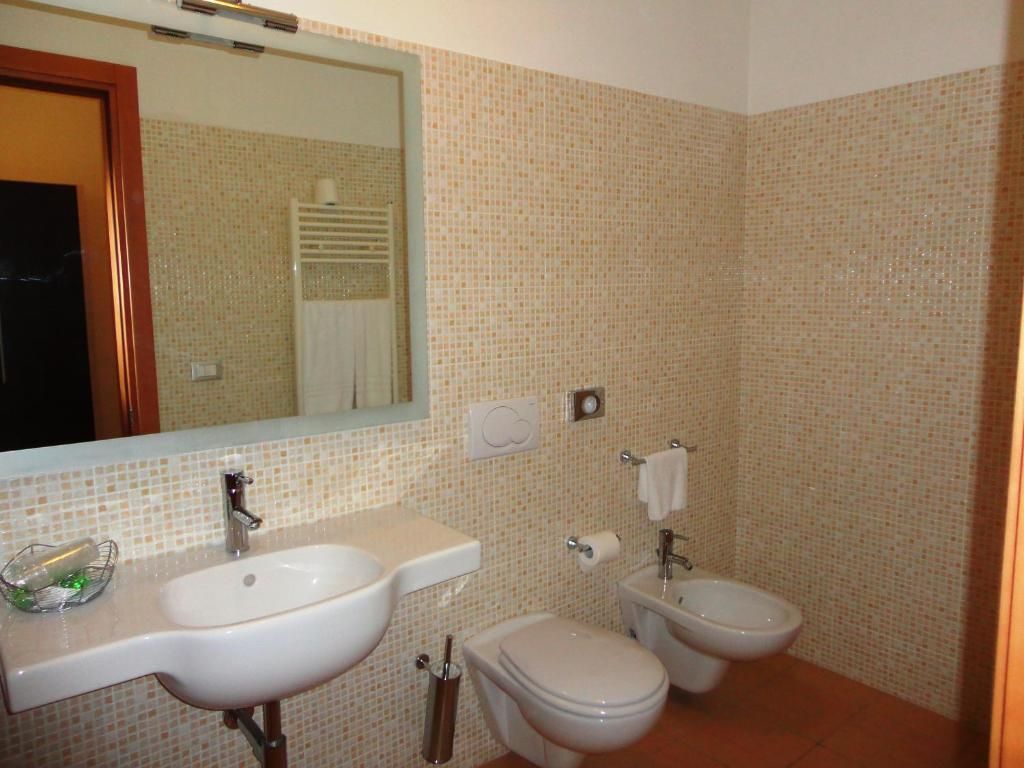 A bathroom with a sink, toilet, and bidet, tiled walls, and a mirror.