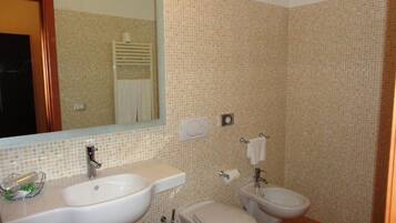 A bathroom with a sink, toilet, and bidet, tiled walls, and a mirror.
