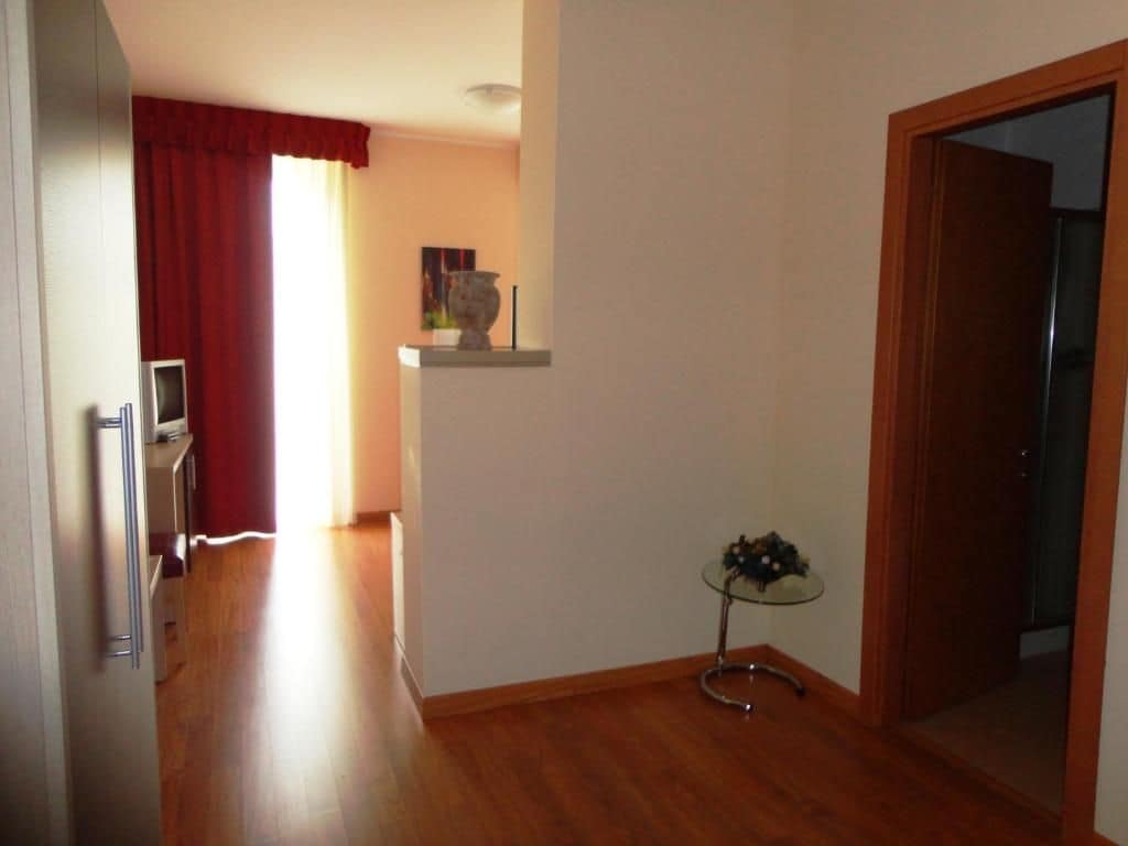 Un pasillo con suelo de madera, una mesa de vidrio con un florero y una puerta que da a otra habitación.