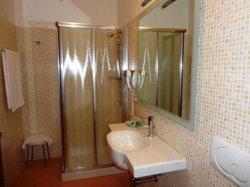 Un bagno con cabina doccia in vetro, un lavabo bianco e una parete rivestita in piastrelle.