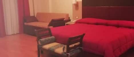 A hotel room with a bed, a desk, a chair, and a lamp.