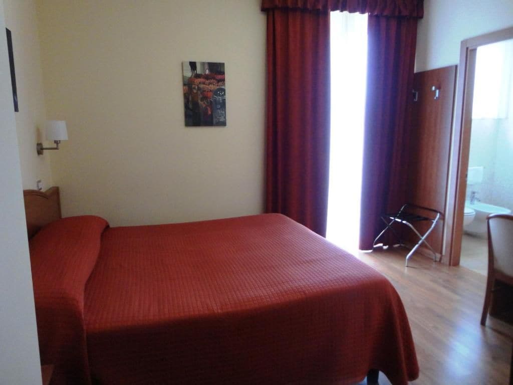 Una stanza con un letto, una sedia, una porta e una finestra con tende.