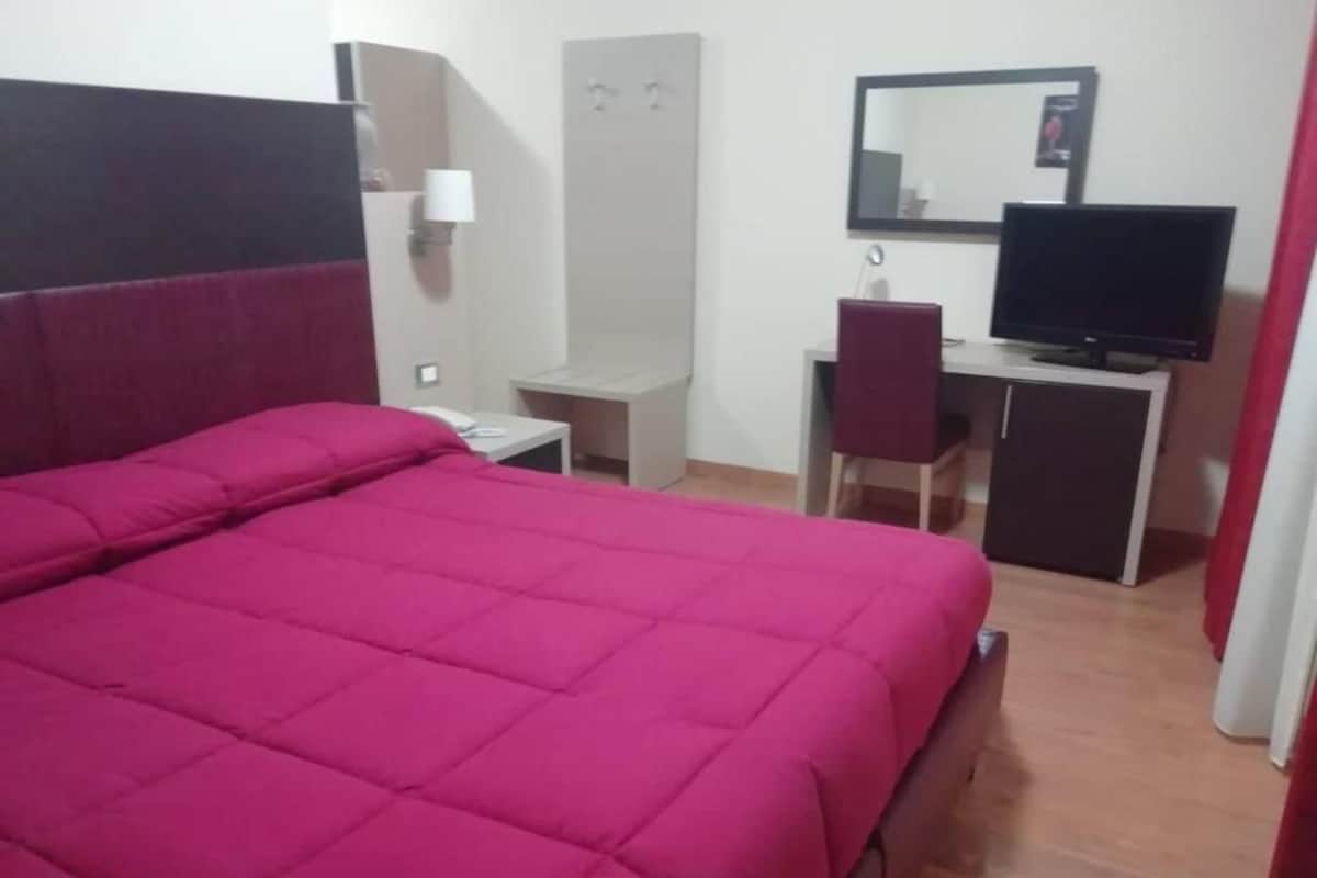 Una habitación con una cama grande, un escritorio con una silla, un televisor y un armario.