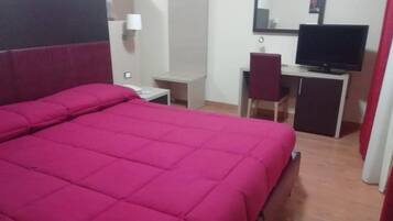 A room with a large bed, a desk with a chair, a television, and a wardrobe.