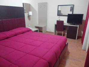Una habitación con una cama grande, un escritorio con una silla, un televisor y un armario.