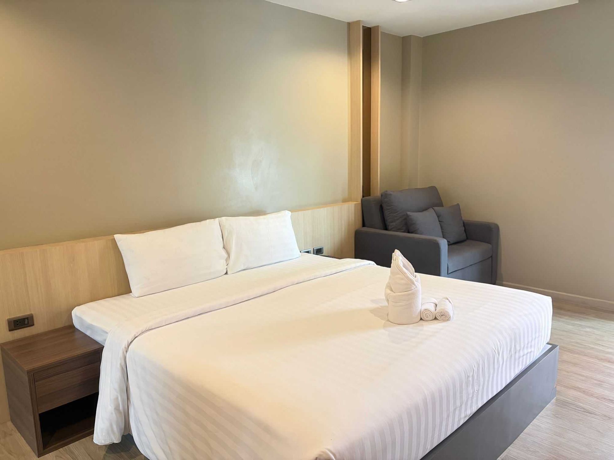 A hotel room with a large bed, a bedside table, a gray sofa, and a wall-mounted TV.
