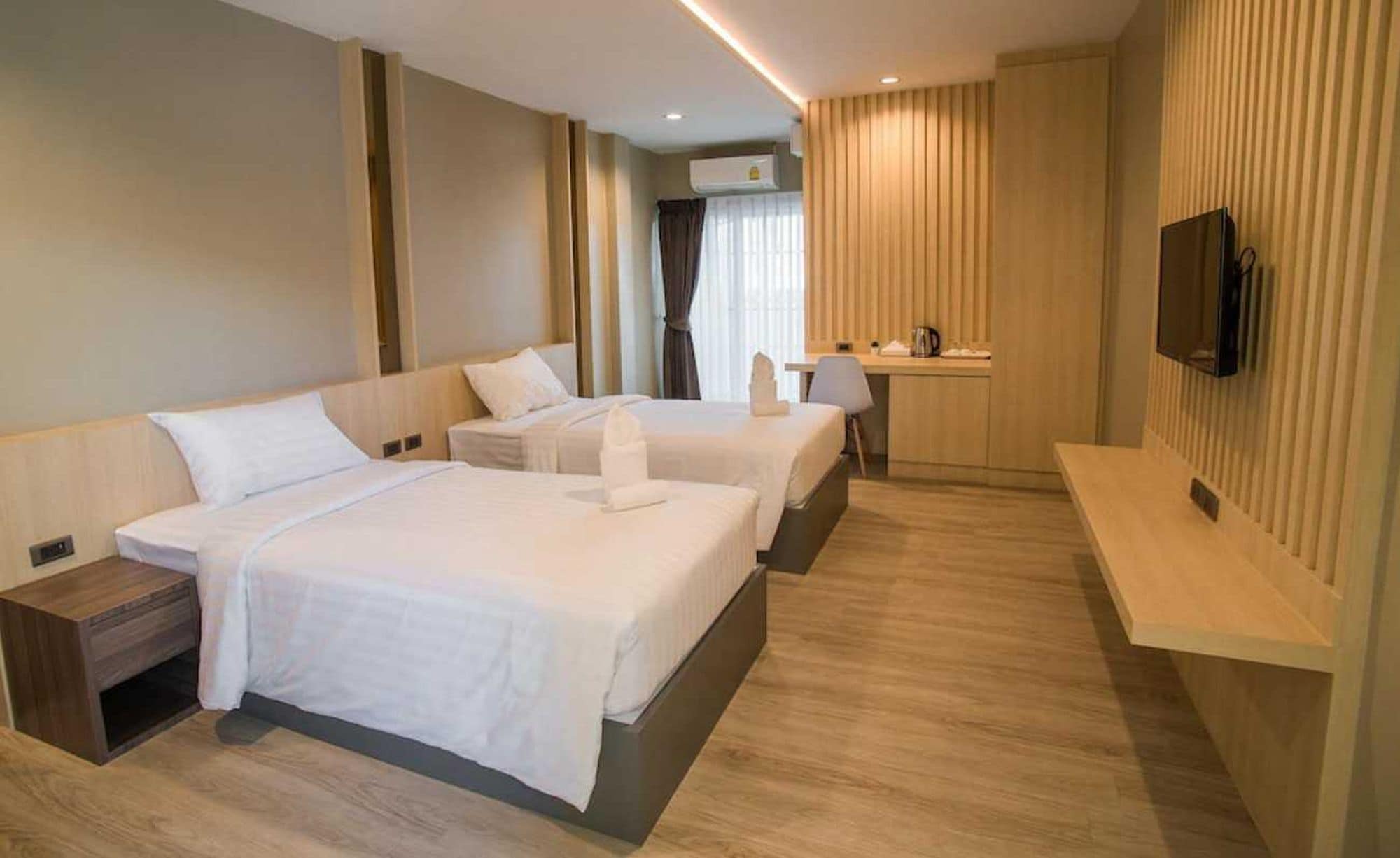 A hotel room with two beds, a desk, a chair, a TV, and a window with curtains.