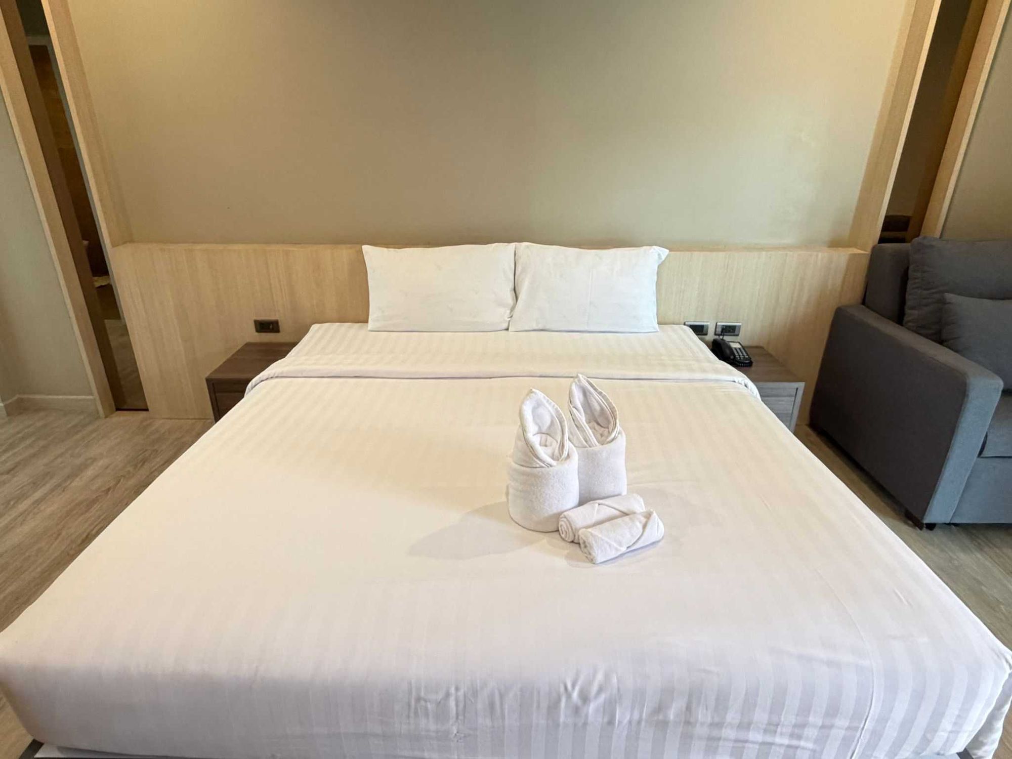 Una habitación de hotel con una cama grande, una mesita de noche con un teléfono y un sillón gris.